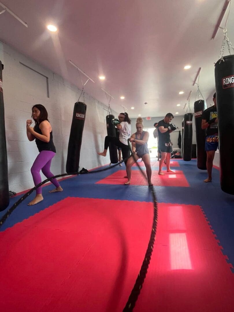 People practicing martial arts in a gym with punching bags and red and blue mats.