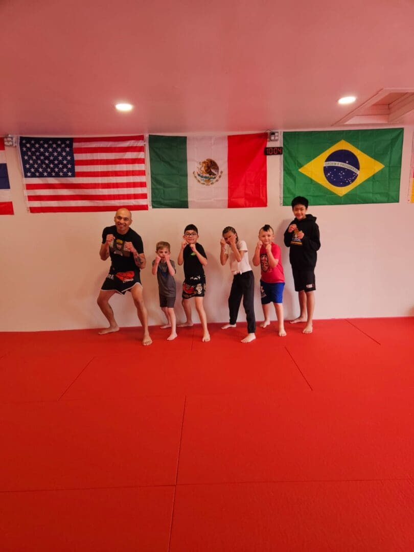 Five people posing in a martial arts gym with American, Mexican, and Brazilian flags on the wall behind them.
